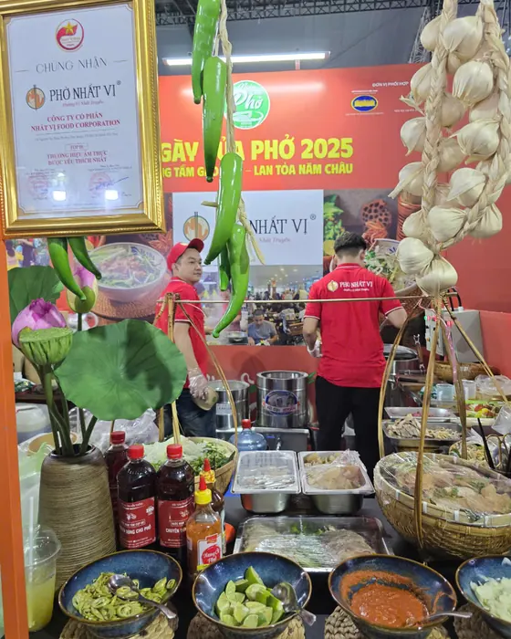 Chai Tôm Cọp Đỏ trên bàn gia vị bên ớt, chanh, tương ớt, sau lưng là băng rôn Ngày của Phở 2025