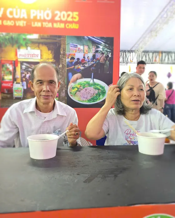 Hai cô chú lớn tuổi ngồi ăn phở trước tấm ảnh Phở Thìn tại lễ hội